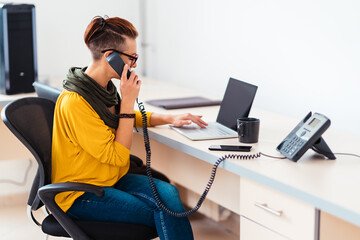 Businesswoman using laptop and landline phone in the office