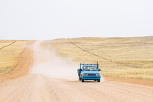 Small Blue Pickup Truck Driving On A Dirt Road In The Countryside