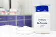 Selective focus of a bottle of sodium carbonate chemical compound or soda ash beside a petri dish with solid crystalline powder substance. White Chemistry laboratory background with copy space.