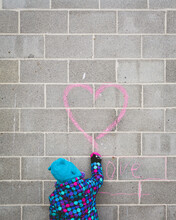 Young Girl Draws Pink Heart With Chalk On Wall Above The Word 'love'