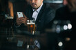 © Sean Locke Photography/Stocksy - Bar: Businessman Checks Texts While Sitting At Bar With Friend