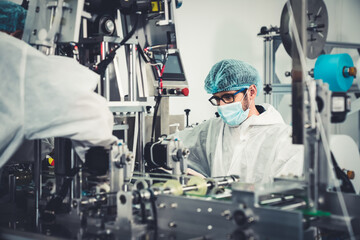 Production line worker with face mask working in electronic factory . Concept of protective action and quarantine to stop spreading of Coronavirus Disease 2019 or COVID-19 .