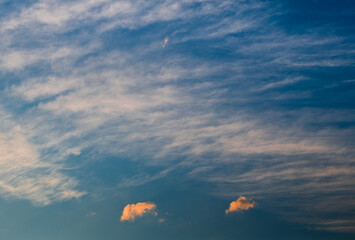 Two small orange clouds in the blue sky before sunset