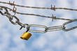 © IHX - Padlock and steel chains with barbed wire against blue clouded sky symbolizing lockdown