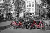 Fototapeta Uliczki - A picture of two red bikes on the bridge over the channel in Amsterdam. The background is black and white. 