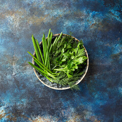 Wall Mural - Plate with parsley, dill, cilantro, green onions on blue background