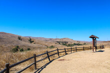 Vast Open Mountain Range Landscape Covered With Dry Brush And Green Trees With Blue Sky And A Wooden Fence At Chino Hills State Park In Chino Hills California