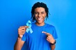 © Krakenimages.com - Young african american man holding blue ribbon smiling happy pointing with hand and finger