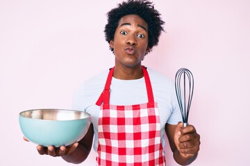 Handsome african american man with afro hair cooking using baker whisk looking at the camera blowing a kiss being lovely and sexy. love expression.