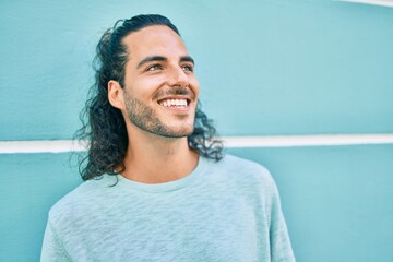 Young hispanic man smiling happy looking to the side leaning on the wall