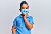 Little Boy Hispanic Kid Wearing Medical Mask Smiling Looking Confident At The Camera With Crossed Arms And Hand On Chin. Thinking Positive.