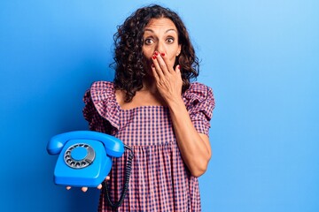 Wall Mural - Middle age beautiful woman holding vintage telephone covering mouth with hand, shocked and afraid for mistake. surprised expression