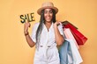 © Krakenimages.com - Young african american woman with braids holding shopping bags and sale banner winking looking at the camera with sexy expression, cheerful and happy face.