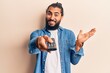 © Krakenimages.com - Young arab man holding television remote control celebrating achievement with happy smile and winner expression with raised hand