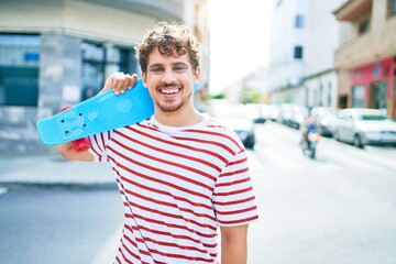 Young caucasian skater man smiling happy holding skate walking at street of city.