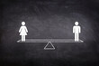 Gender Equality Concept : Male and female figure icon symbols balancing on seesaw or balance scales on chalkboard.