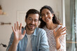 Close up headshot screen view of smiling young Caucasian couple look at screen talk on video call. Portrait of happy millennial man and woman wave greet have webcam digital conversation at home.