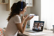 © fizkes - Happy Caucasian young woman look at laptop screen talk chat on video call with African American man husband. Smiling female in headphones have webcam digital virtual communication with friend.