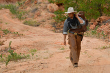A Young Cowboy Carrying A Saddle Down A Small Dirt Road. In One Of The Mines