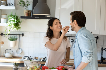 Overjoyed millennial Caucasian couple have fun preparing delicious food in renovated modern design kitchen. Happy young man and woman tenants enjoy cooking together healthy dinner salad at home.