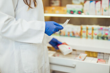 Close up shot of female pharmacist hands in protective gloves working at pharmacy. Medical healthcare concept.