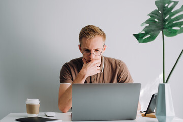 pensive caucasian man in glasses mobile developer, programmer writes program code on a laptop comput