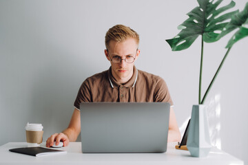 focused caucasian man in glasses mobile developer, programmer writes program code on a laptop comput