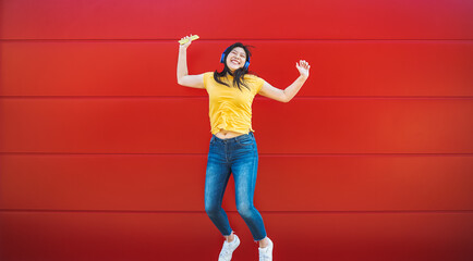 Wall Mural - Happy Asian girl jumping while listening music playlist with wireless headphones - Young woman having fun dancing outdoor - Youth millennial generation lifestyle people and technology concept