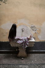 Girl In Dress With Long Black Hair Sitting On Ancient Fountain In Italy