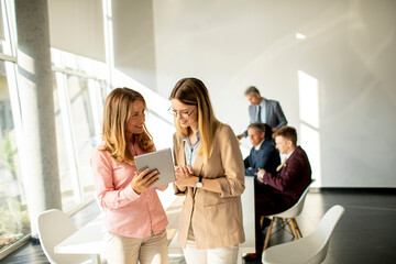 Two smiling women looking on digital tablet at the office