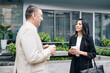 © DragonImages - Smiling beautiful young Asian businesswoman listening to ideas of her senior colleague when they are drinking take out coffee outdoors