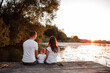 © Andriy Medvediuk - Young parents and their little son sitting on the wooden pier near the lake, at sunset on summer day.