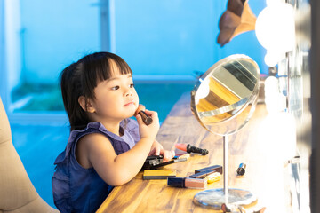 Pretty little toddler girl is applying blush on cheek