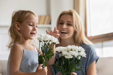 Happy delighted elder and younger sisters receiving flowers from father and brother on March 8, adorable smiling young mommy and little girl daughter pleased by husband and dad surprise on Women Day