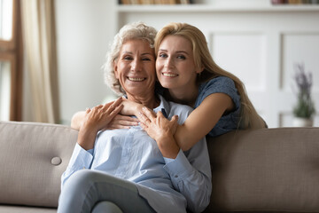 Wife of my son is like daughter to me. Happy young woman embracing from back senior mother in law feeling respect and love, friendly family mature mom and adult daughter hugging and looking at camera