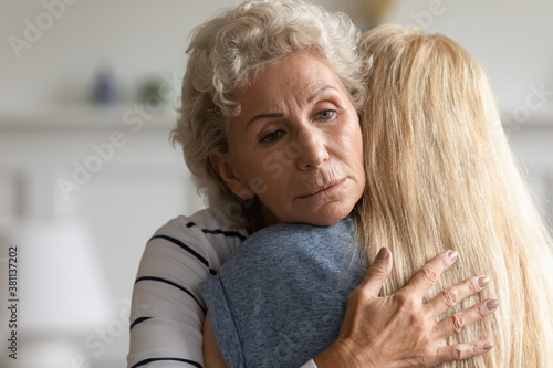 Mommy is with you, dear. Caring understanding aged mother embracing her adult kid girl with compassion and kindness in eyes, loving old granny hugging tight grown granddaughter hiding anxiety on face