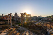 Silent dawn in the Roman Forum, Rome. The sun's rays appear from the temple of Saturn and illuminate the buildings, the Arch of Severus, the temple of Vesta, the Arch of Titus, the Coliseum. Italy.
