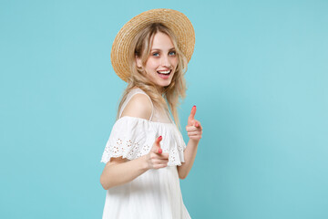 Wall Mural - Side view of cheerful excited funny young blonde woman 20s wearing white summer dress hat standing pointing index fingers on camera isolated on blue turquoise colour background, studio portrait.