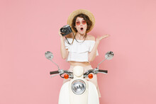 Shocked Young Brunette Woman 20s Wearing White Summer Clothes Hat Eyeglasses Hold In Hand Retro Vintage Photo Camera Sitting Driving Moped Isolated On Pastel Pink Colour Background Studio Portrait.