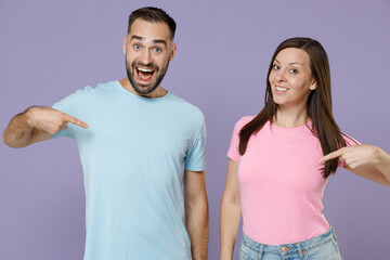 Wall Mural - Smiling excited young couple two friends man woman in blue pink empty blank design t-shirts standing pointing index fingers on themselves isolated on pastel violet color background studio portrait.