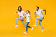 © ViDi Studio - Full length portrait of cheerful funny young parents mom dad with child kid daughter teen girl in basic t-shirts jumping like running isolated on yellow background studio portrait. Family day concept.