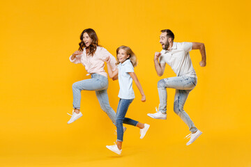 Wall Mural - Full length portrait of cheerful funny young parents mom dad with child kid daughter teen girl in basic t-shirts jumping like running isolated on yellow background studio portrait. Family day concept.