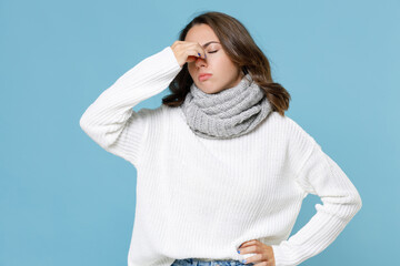 Sick tired young woman in white sweater gray scarf put hand on nose keeping eyes closed isolated on blue background studio portrait. Healthy lifestyle ill sick disease treatment cold season concept.