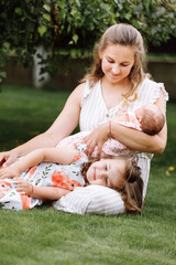 portrait of loving mother and two adorable kids. little girl and newborn baby girl with mom outdoors on summer day. Happy family spent time together in the park