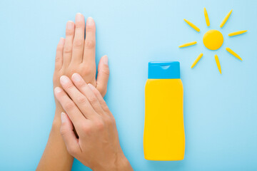 Wall Mural - Young woman hands, yellow tube of sunscreen and sun shape on light blue table background. Pastel color. Care about skin protection in hot summer. Point of view shot. Closeup. Top down view.