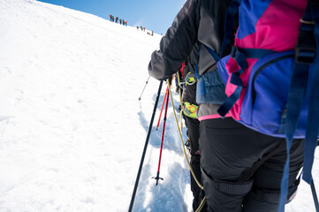 Rope team member point of view with mountaineers walking on snow and ice in sunny weather.