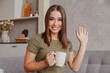 © vladdeep - Portrait of pleasant young woman with mug looking at camera, waving hello. Pretty millennial lady communicating with parents via video call. Attractive female blogger greeting followers.