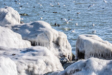 Jetty With Ice Covered Rocks With Sea Birds In The Blue Water.
