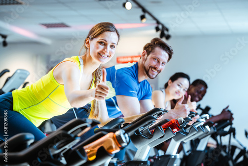 Woman showing thumbs up sign exercising of fitness bike in gym