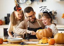 Happy Family   Father And Children Prepare For Halloween By Carving Pumpkins At Home In Kitchen.